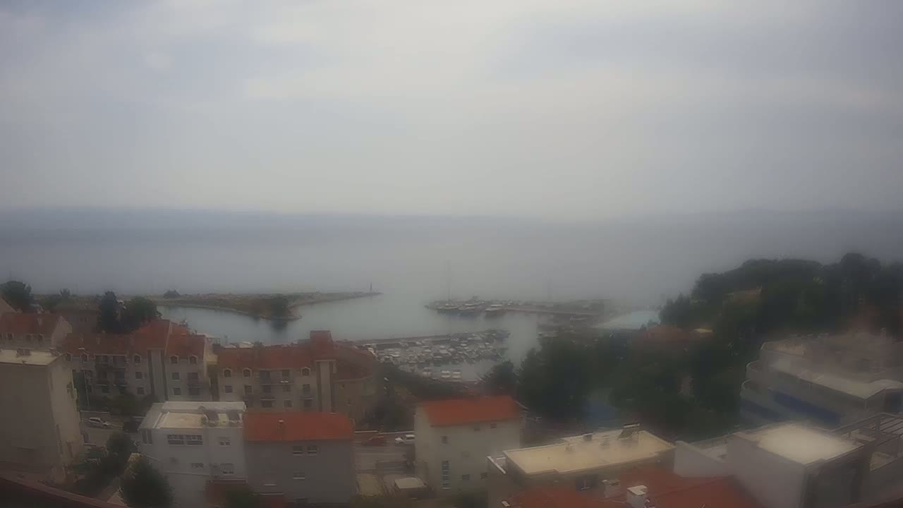 A hazy, sunny day overlooks a coastal town with red-roofed buildings surrounding a harbor filled with boats.