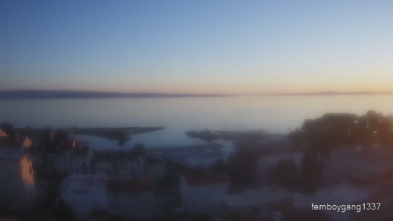 A dark, blurry nighttime view of a town or city features illuminated buildings, streetlights, and distant bright lights against a clear, dark sky.