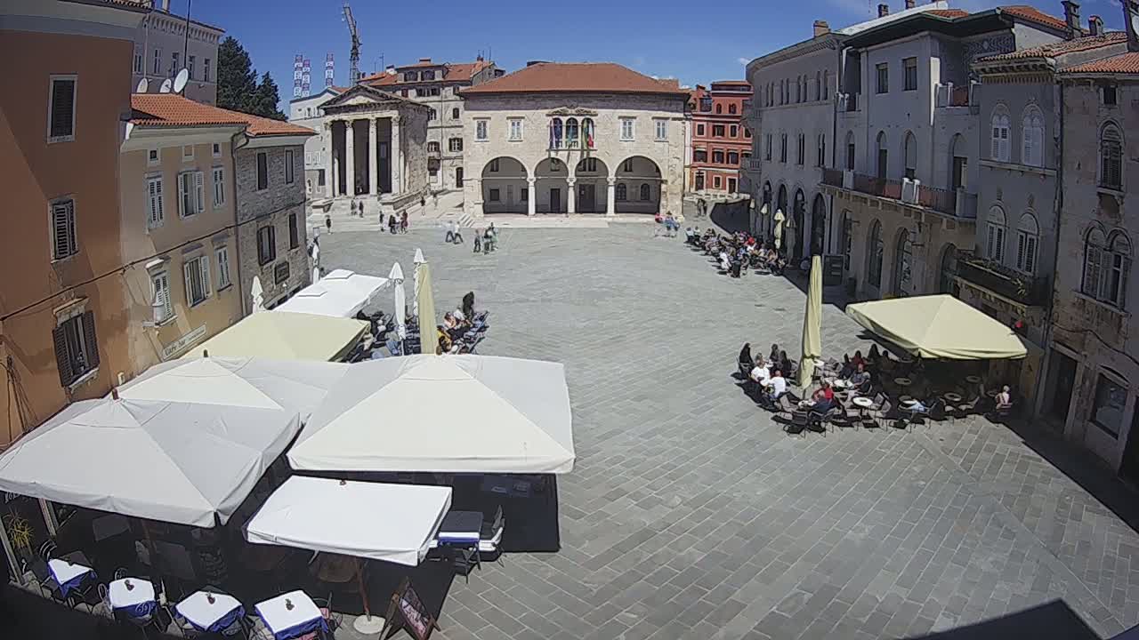 A large town square with several outdoor cafes under umbrellas on a sunny day.