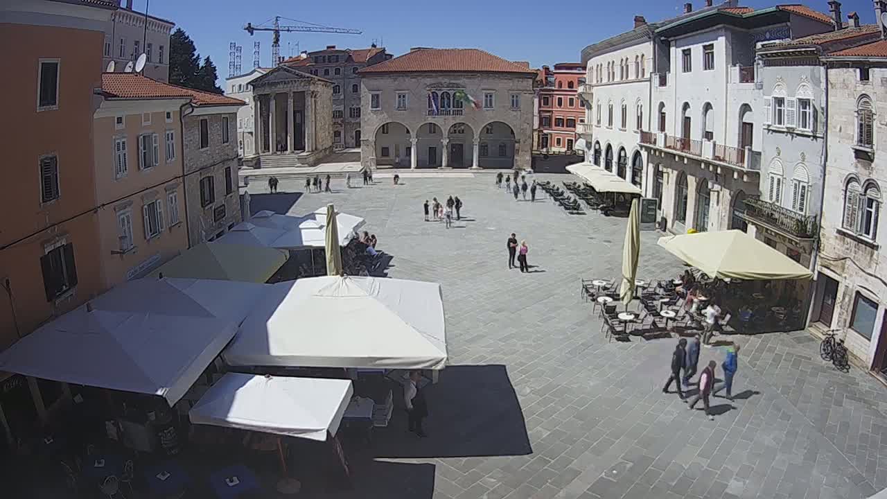 A sunny town square with several outdoor cafes, surrounded by old buildings.
