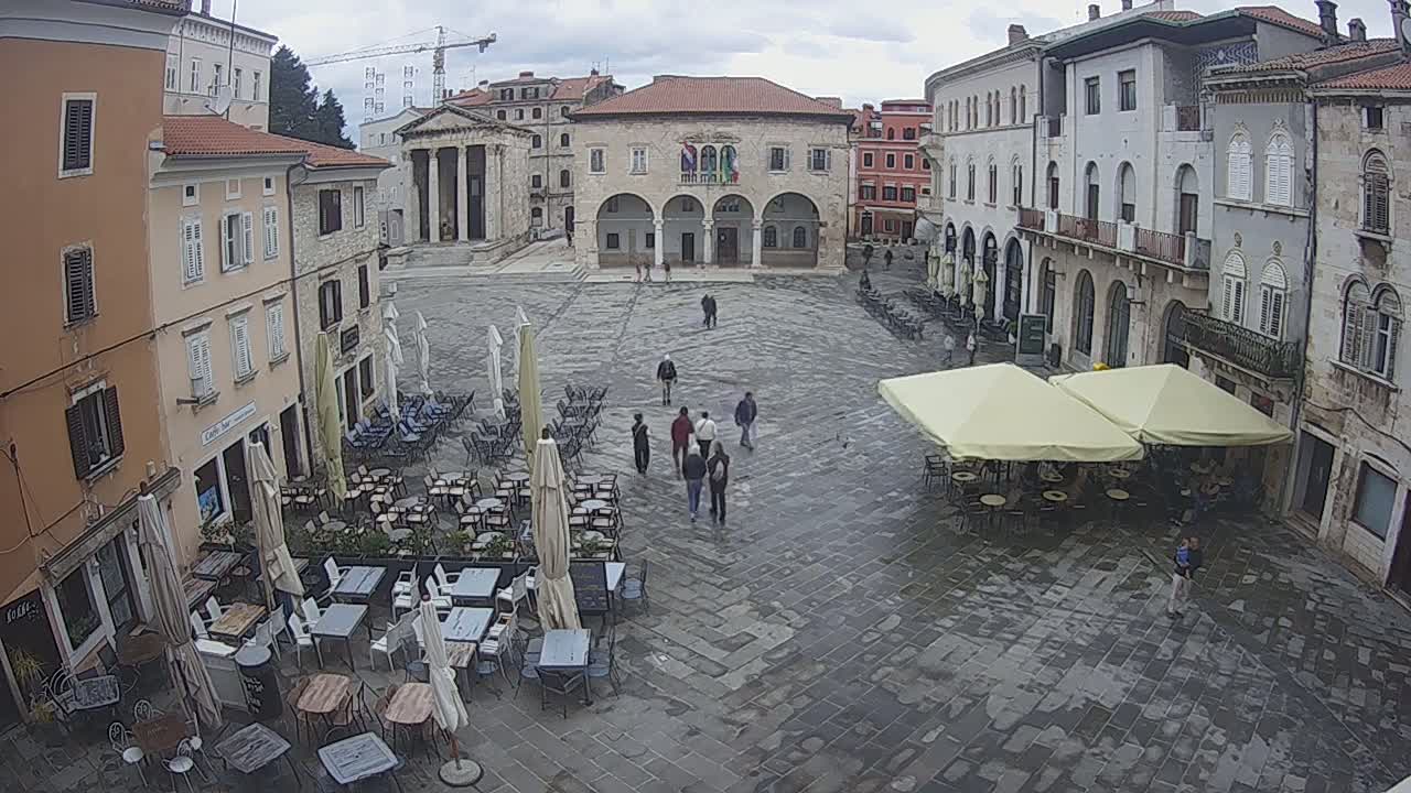 A large town square with several outdoor cafes and historical buildings is seen on an overcast day.