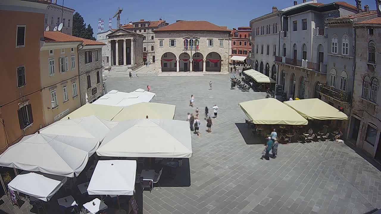A town square with several outdoor cafes under umbrellas on a sunny day.