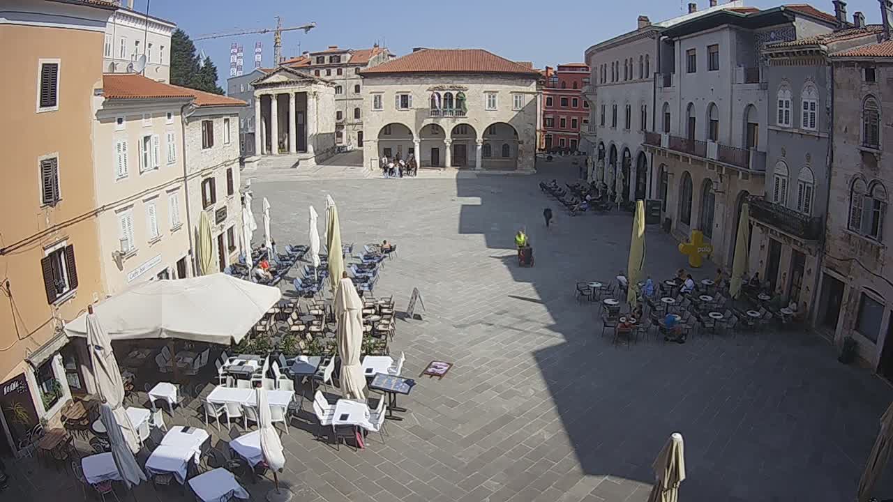 A sunny day reveals a large town square with several outdoor cafes surrounded by historic buildings.
