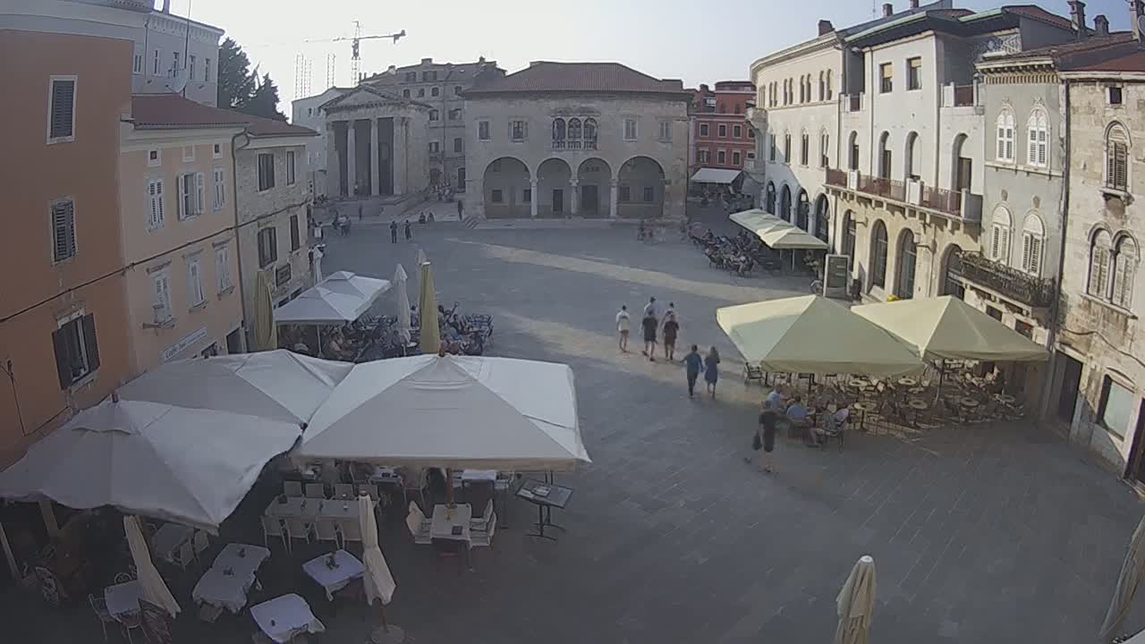 A town square with several outdoor cafe umbrellas and a few people walking around on a sunny day.