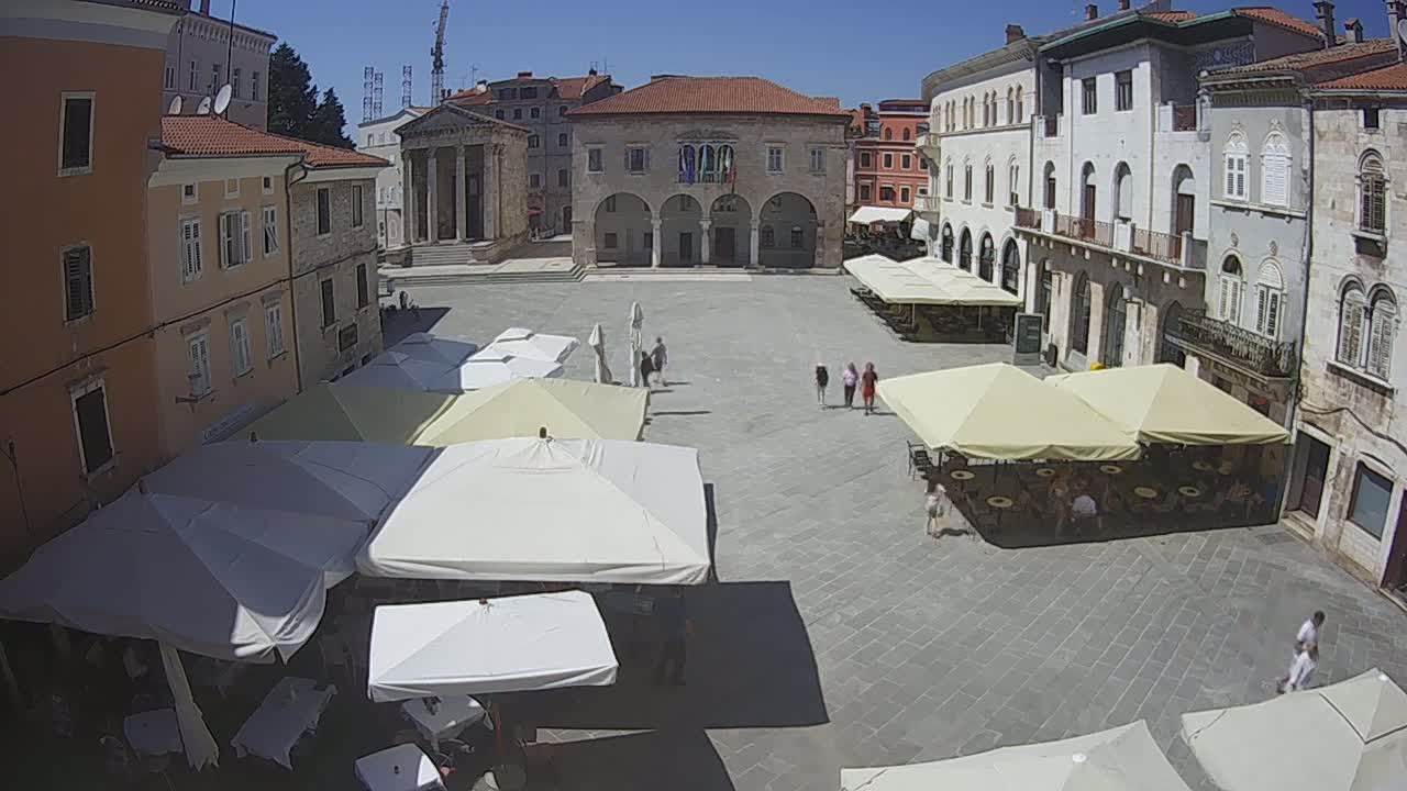 A large town square with several outdoor cafes under umbrellas on a sunny day.