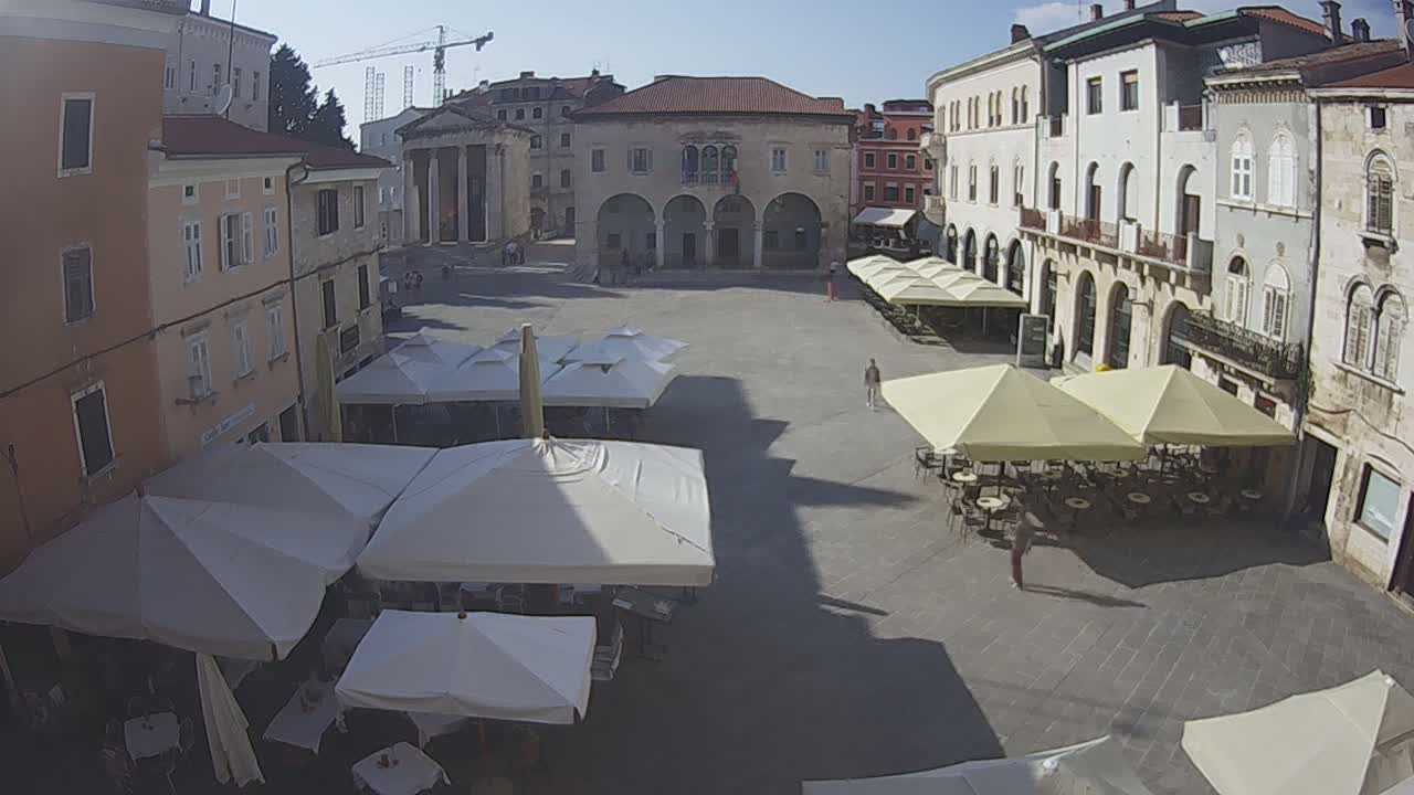 A sunny day in a town square with several outdoor cafes under umbrellas, surrounded by historic buildings.