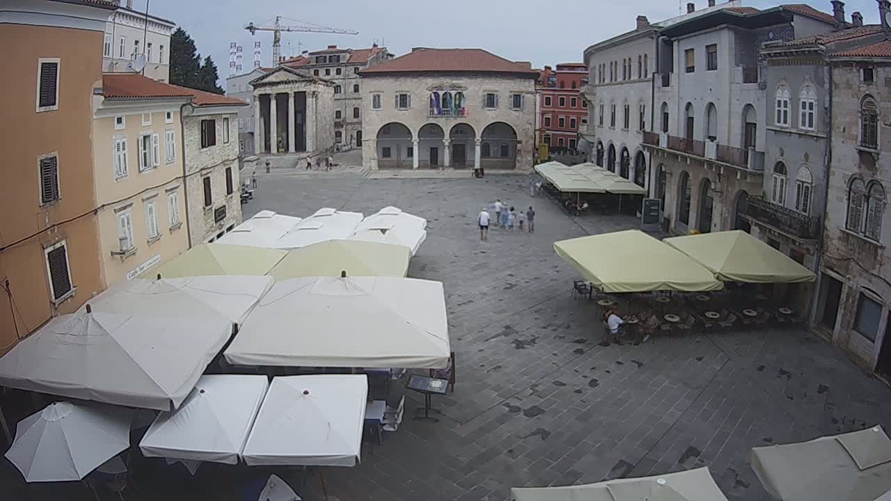 A town square with several outdoor cafe umbrellas and stone buildings, under an overcast sky.