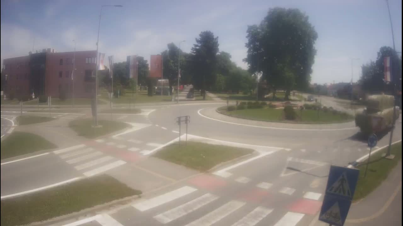 A roundabout intersection on a sunny day with a large truck carrying bales of hay turning onto the road.