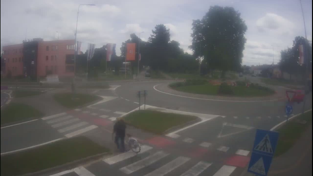 A person on a bicycle crosses a pedestrian crossing near a roundabout on an overcast day.
