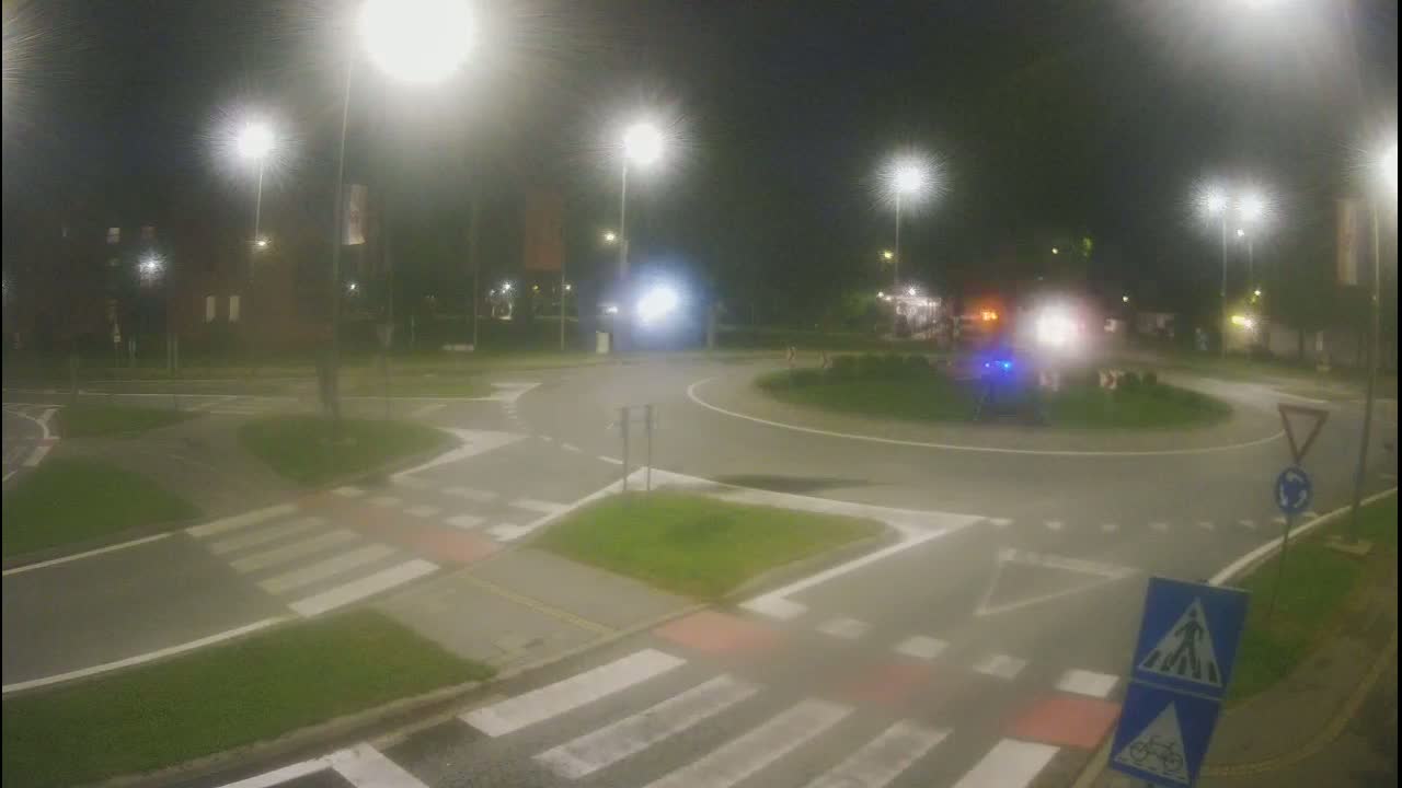 A nighttime view of a roundabout with pedestrian crossings and streetlights, under hazy conditions.