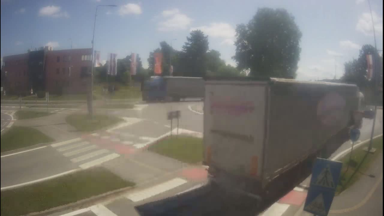 Two semi-trucks are navigating a roundabout on a sunny day.