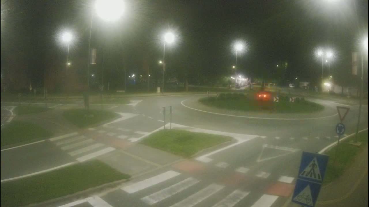 A nighttime view of a roundabout intersection with pedestrian crossings, illuminated by streetlights in hazy conditions.