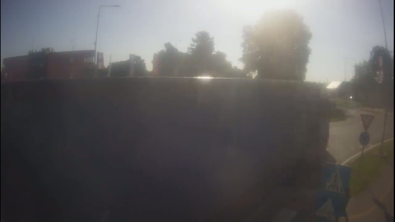 A hazy, sunny day reveals a view of a roadway with buildings and trees in the background, partially obscured by a large dark object in the foreground.
