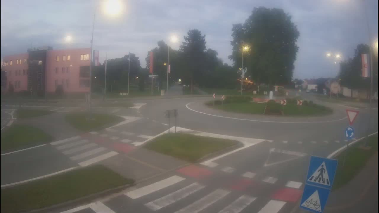 A roundabout at dusk with a pinkish building in the background under hazy conditions.