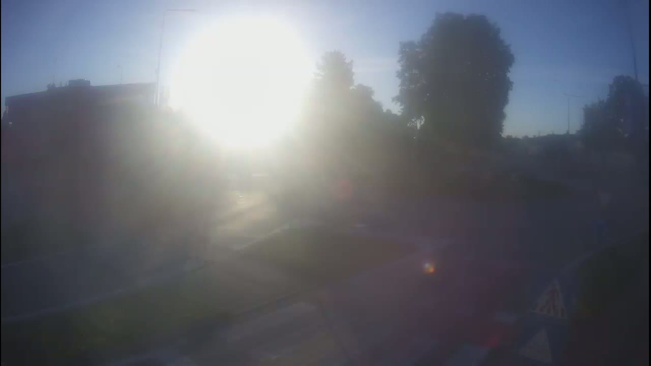 A hazy, sunny day reveals a street scene with buildings and trees partially obscured by bright sunlight and atmospheric conditions.