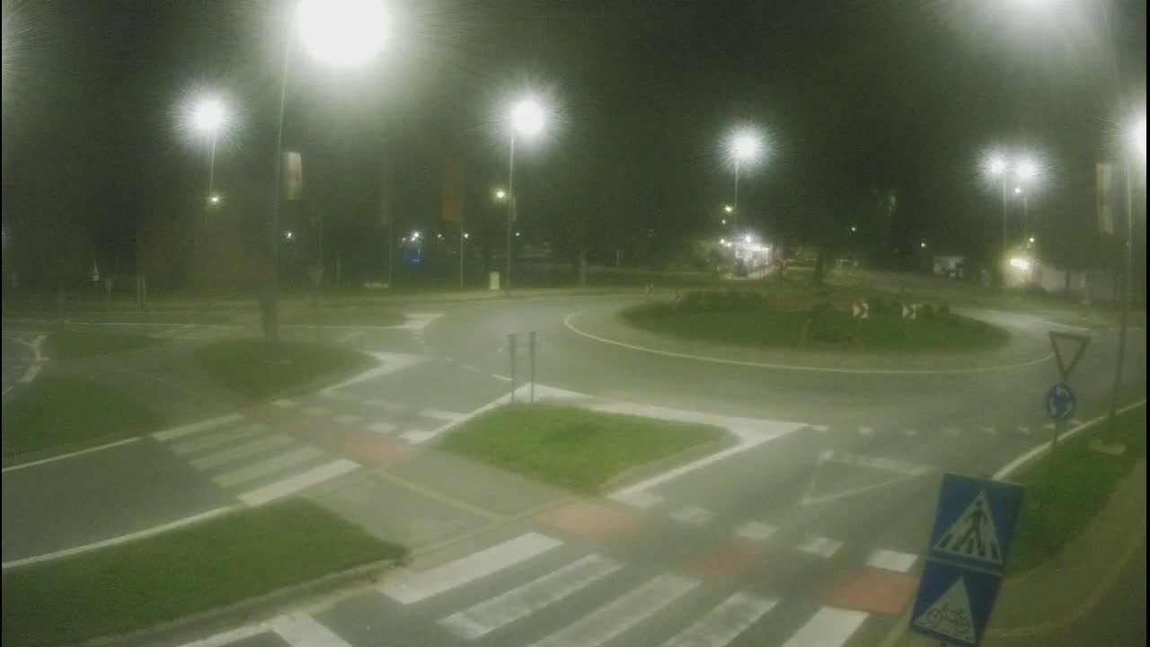 A nighttime view of a roundabout intersection with pedestrian crosswalks, illuminated by streetlights.