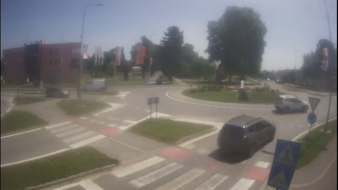 Several cars navigate a roundabout on a sunny day, with green landscaping surrounding the traffic circle.