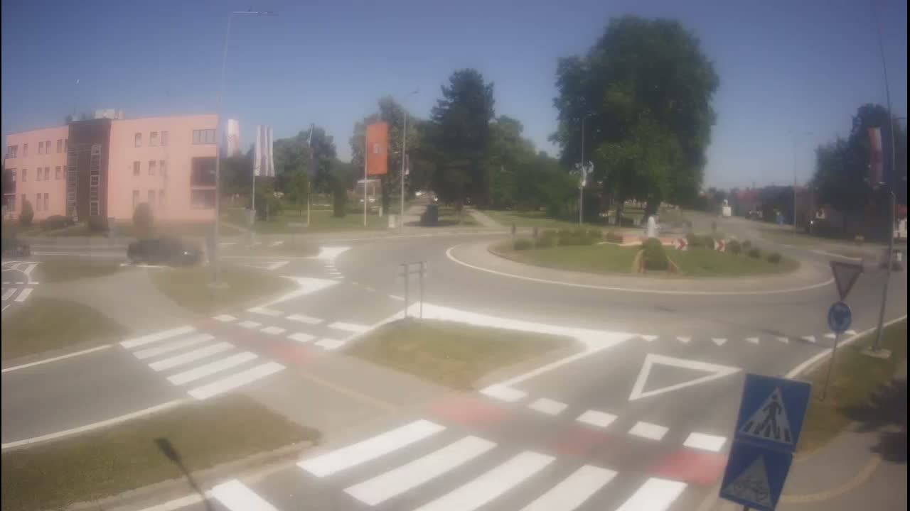 A roundabout intersection with crosswalks and a pink building in the background on a sunny day.