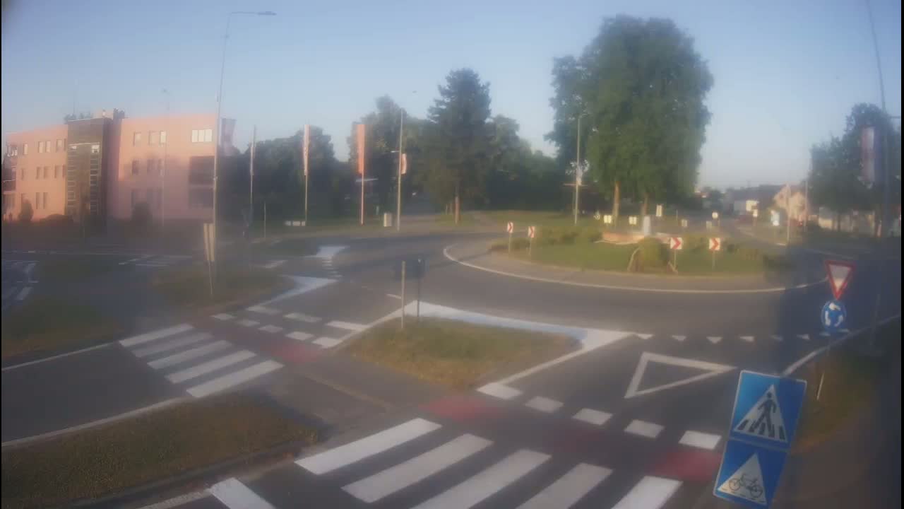 A hazy morning scene shows a roundabout with pedestrian crosswalks and a pink building in the background.