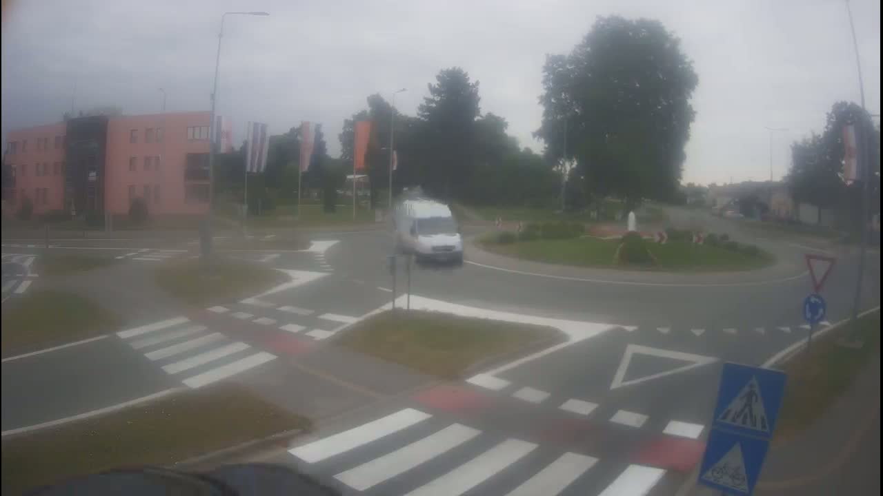 A white van navigates a roundabout on a cloudy day, with pedestrian crossings and street markings clearly visible.