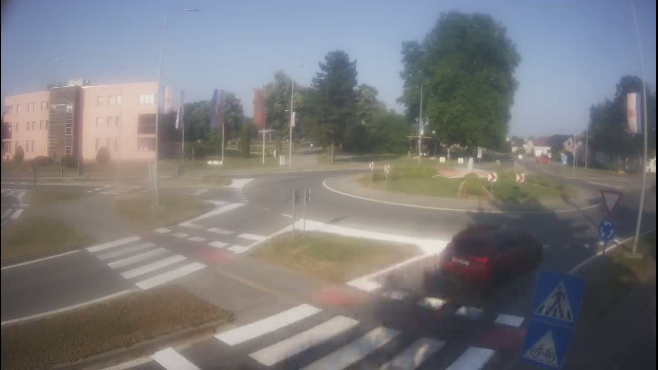 A car drives through a roundabout near a multi-story building on a sunny day.