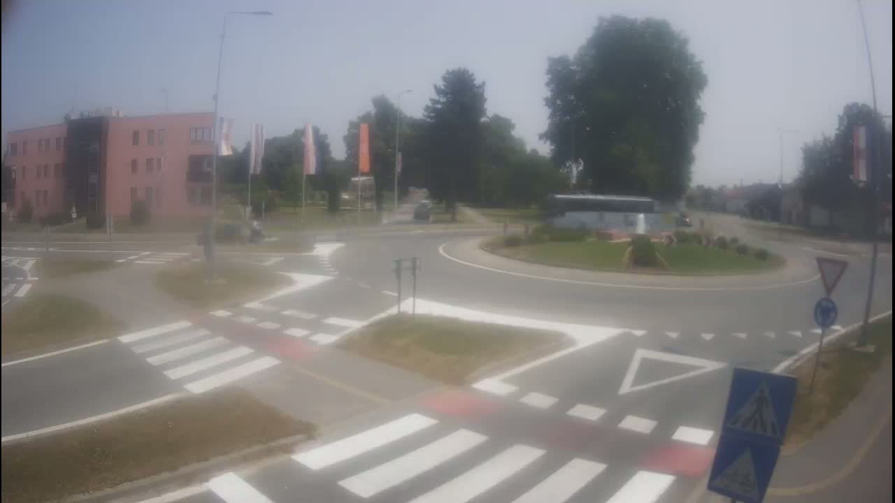 A roundabout with crosswalks and a pink building in the background on a hazy, sunny day.