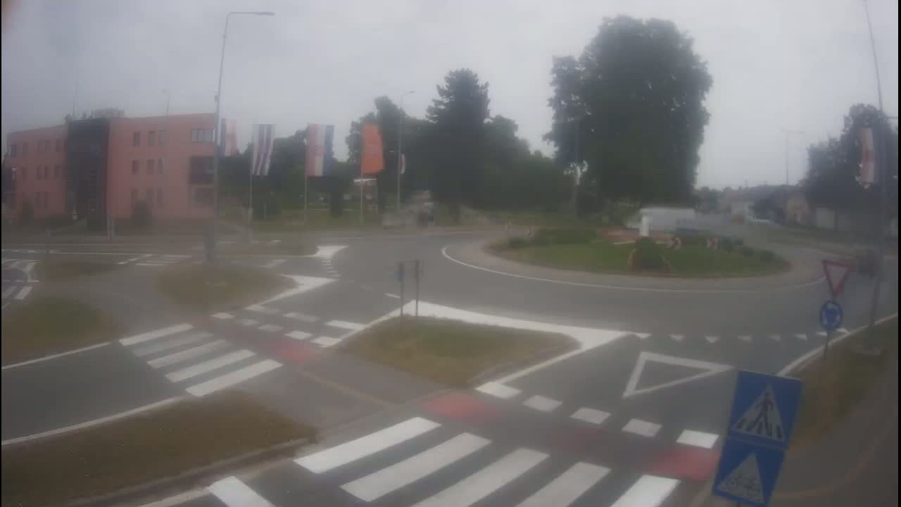 A roundabout with pedestrian crossings and a pink building in the background on a hazy day.