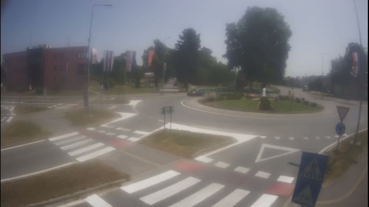 A roundabout with pedestrian crossings and a few cars is visible on a sunny day.