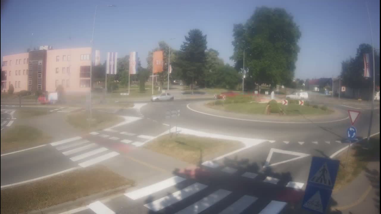 A roundabout with a light-colored building in the background on a sunny day.