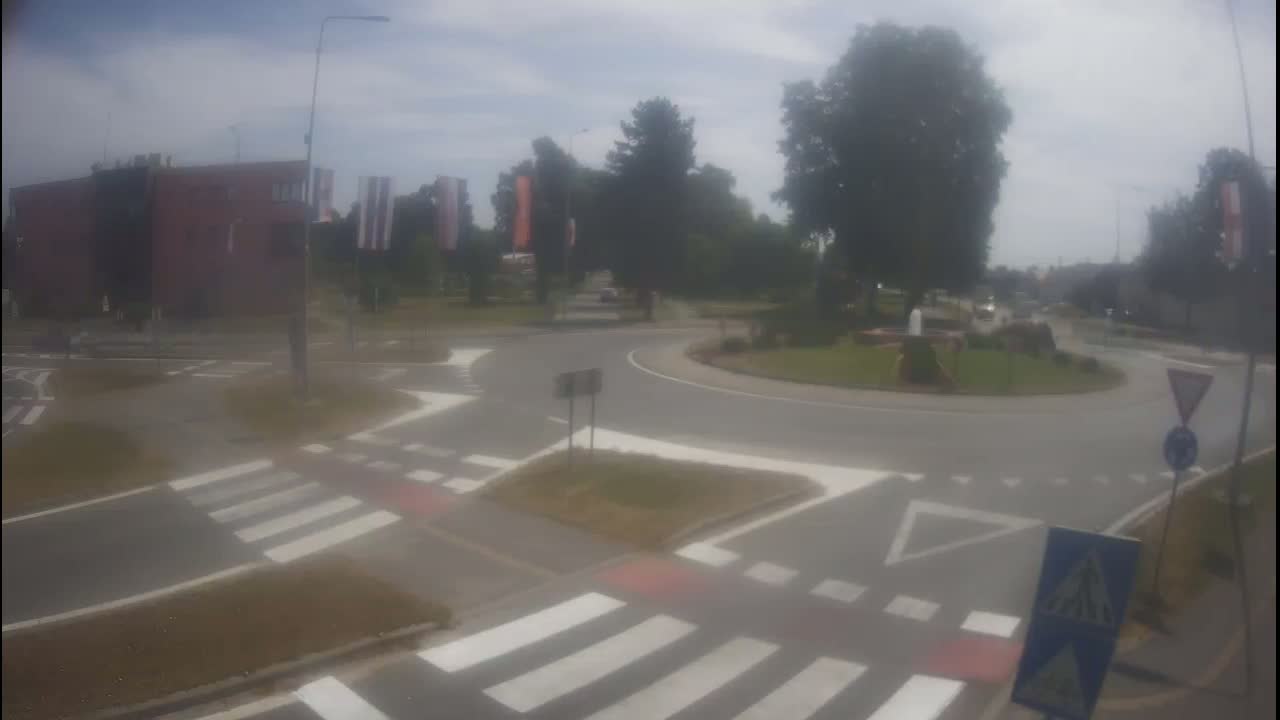 A hazy view of a roundabout with crosswalks and a building in the background on a partly cloudy day.