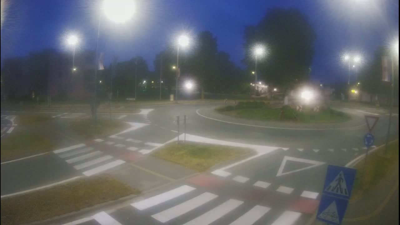 A well-lit roundabout at night, with pedestrian crosswalks and streetlights illuminating the scene under a clear, dark blue sky.