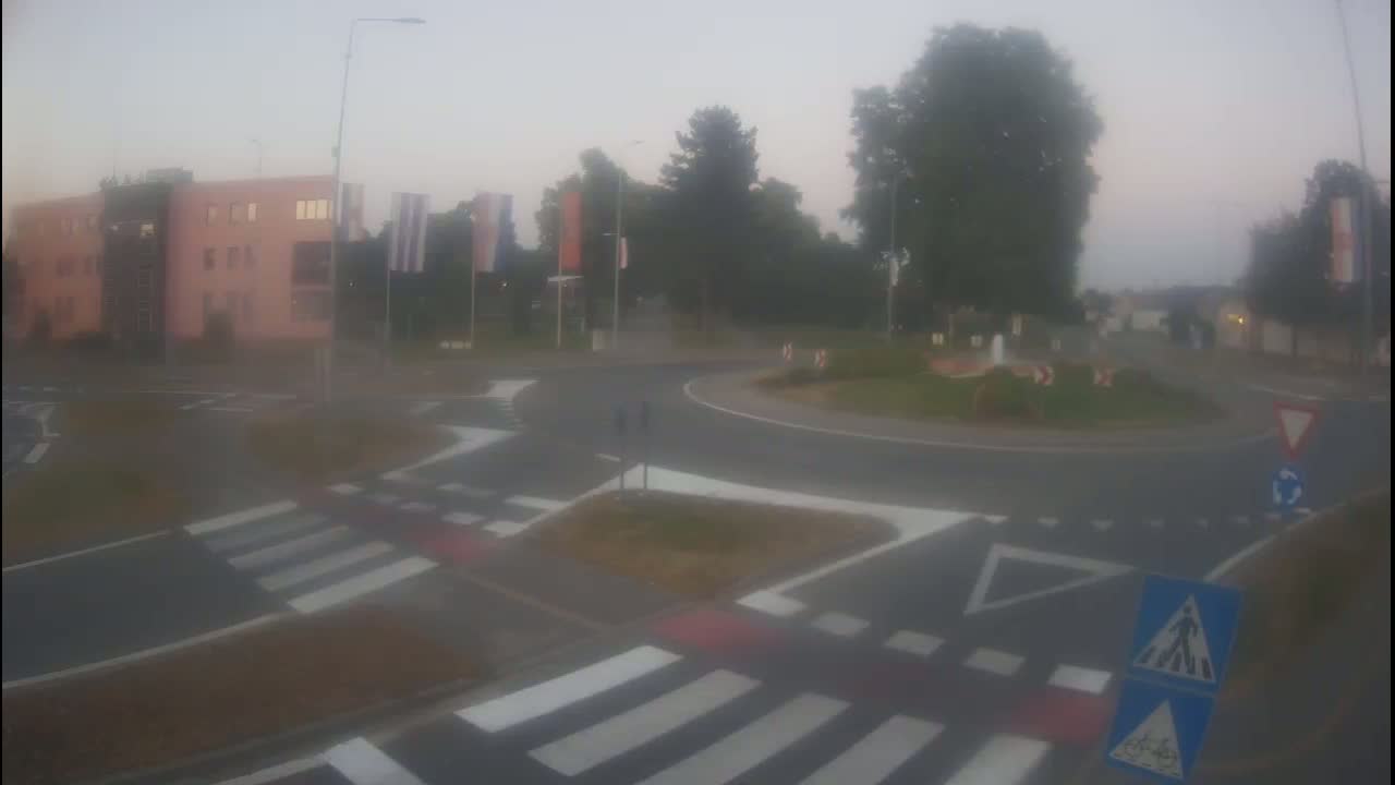 A foggy view of a roundabout with pedestrian crosswalks and a pink building in the background.