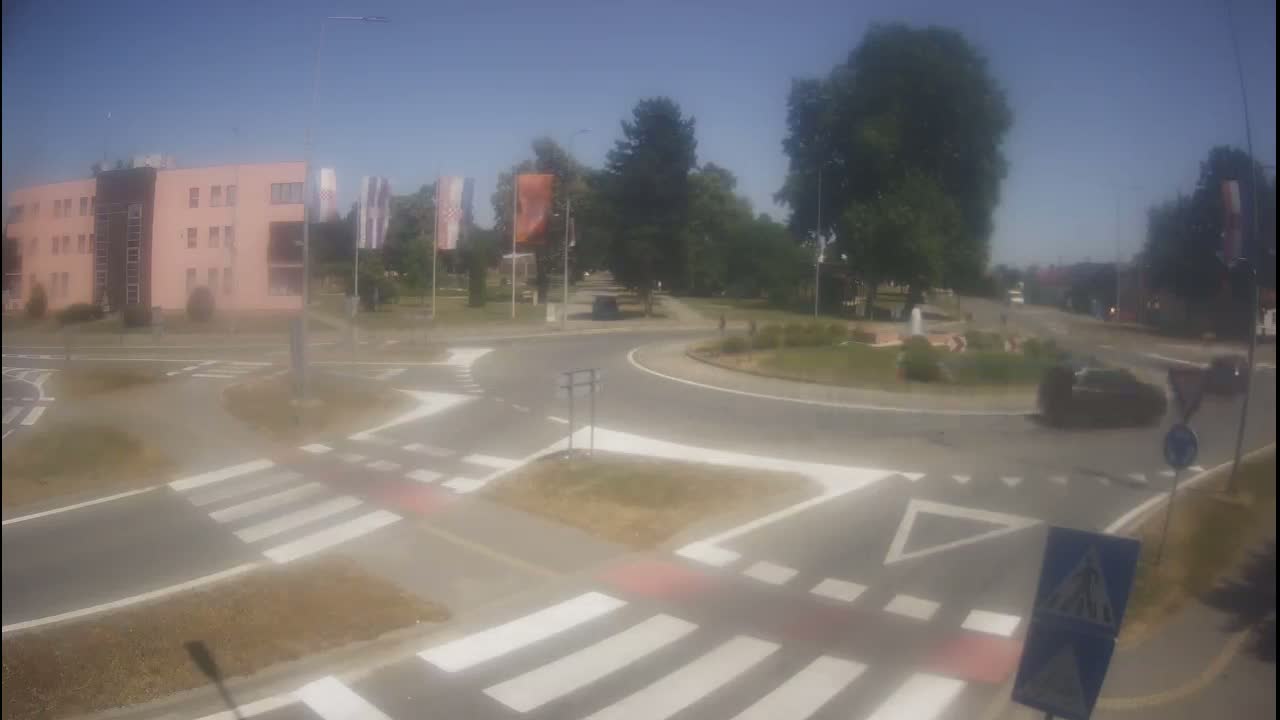 A roundabout with crosswalks and a light-pink building in the background on a sunny day.