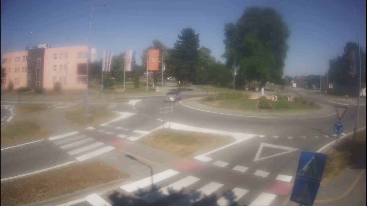 A roundabout with crosswalks and a light pink building in the background on a sunny day.