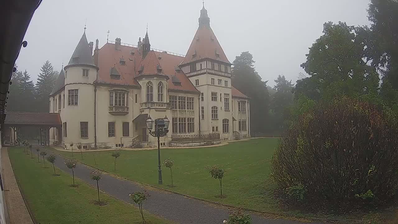 A large, turreted castle stands on a grassy lawn in foggy weather.