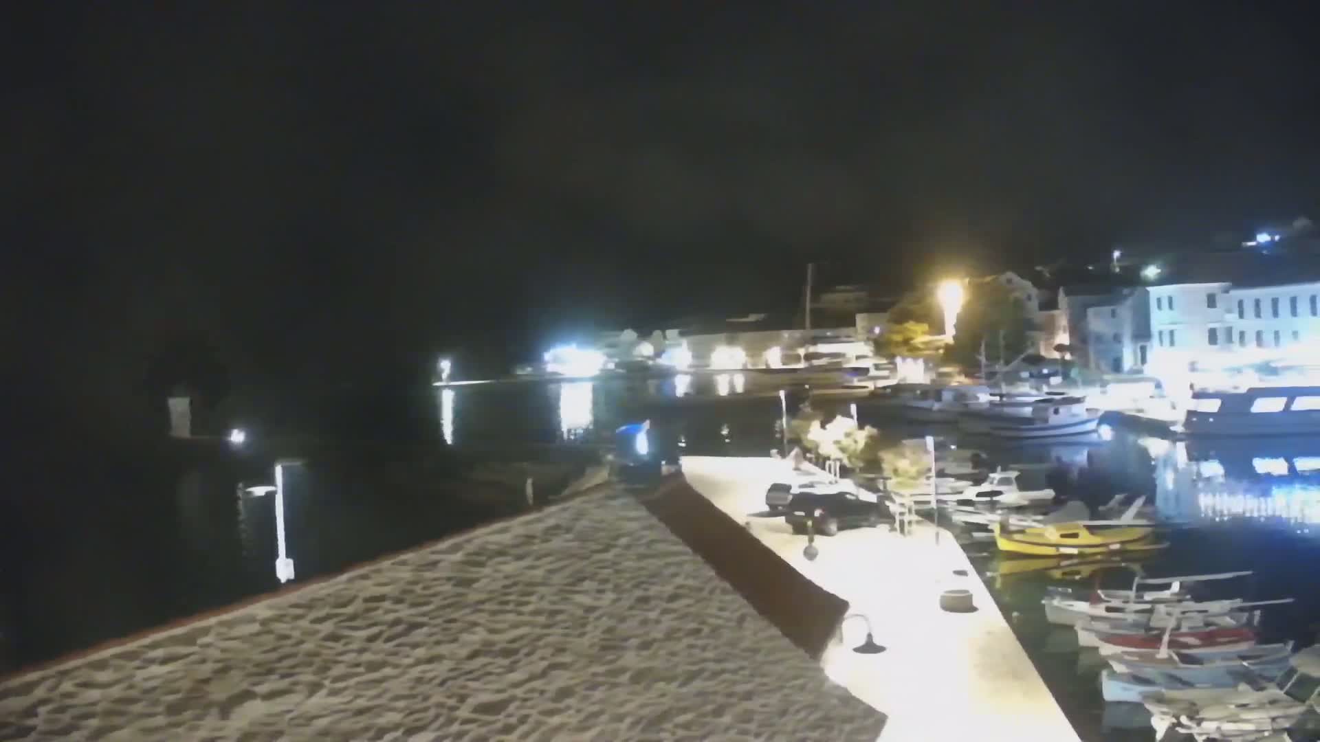A nighttime view of a harbor filled with docked boats and illuminated buildings along the waterfront.