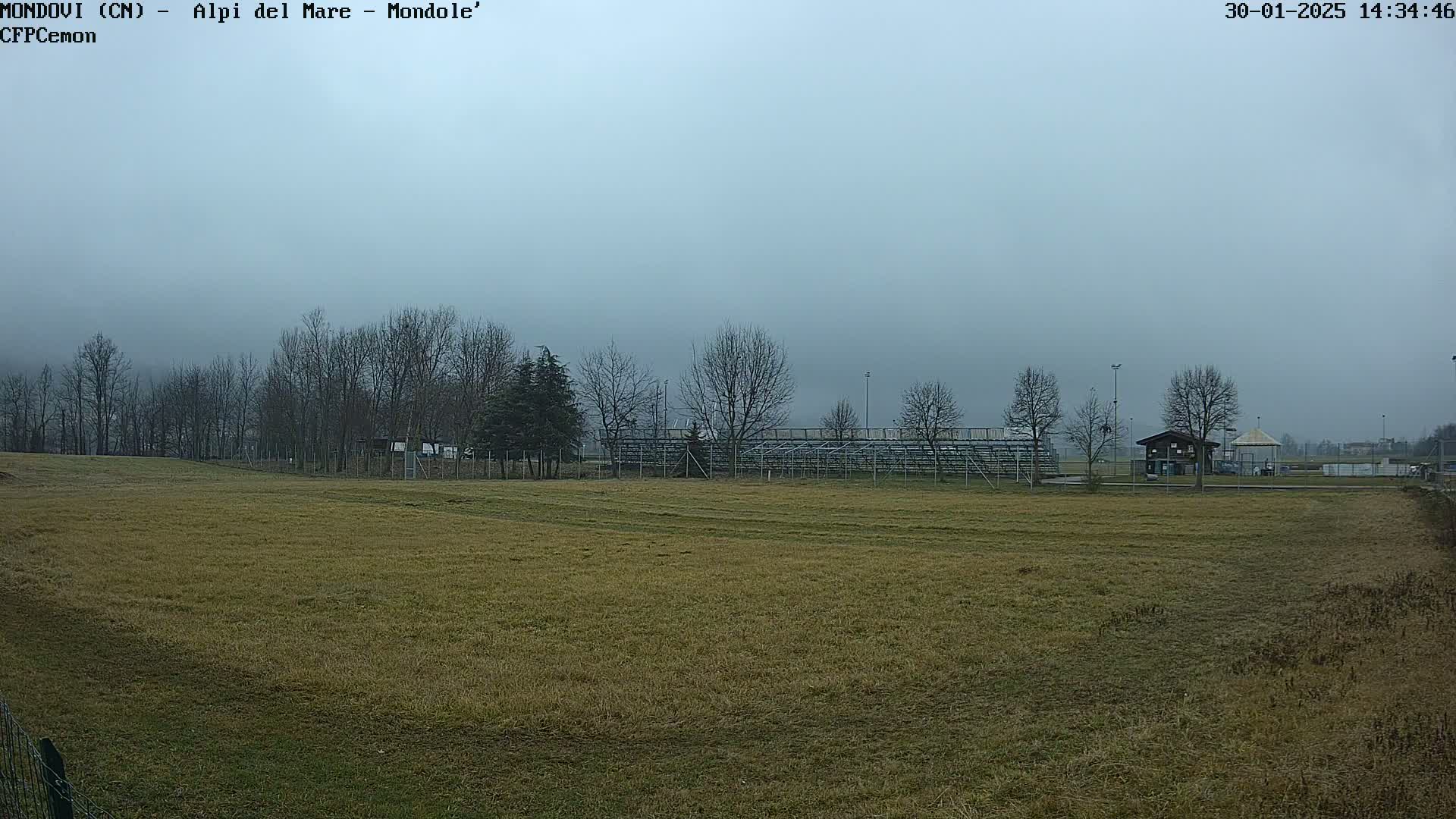 A large, grassy field stretches out before empty bleachers under a hazy, overcast sky.