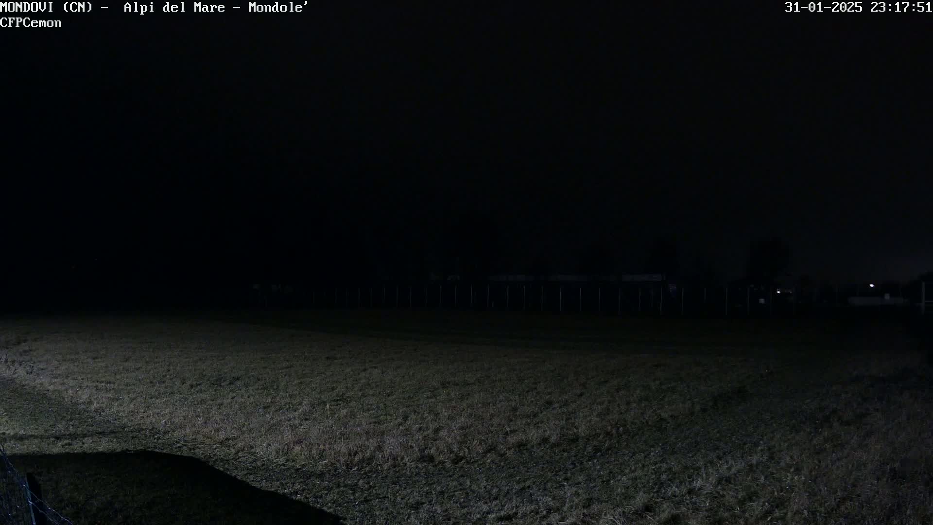 A dark, nighttime view of a grassy field with a fence in the background.