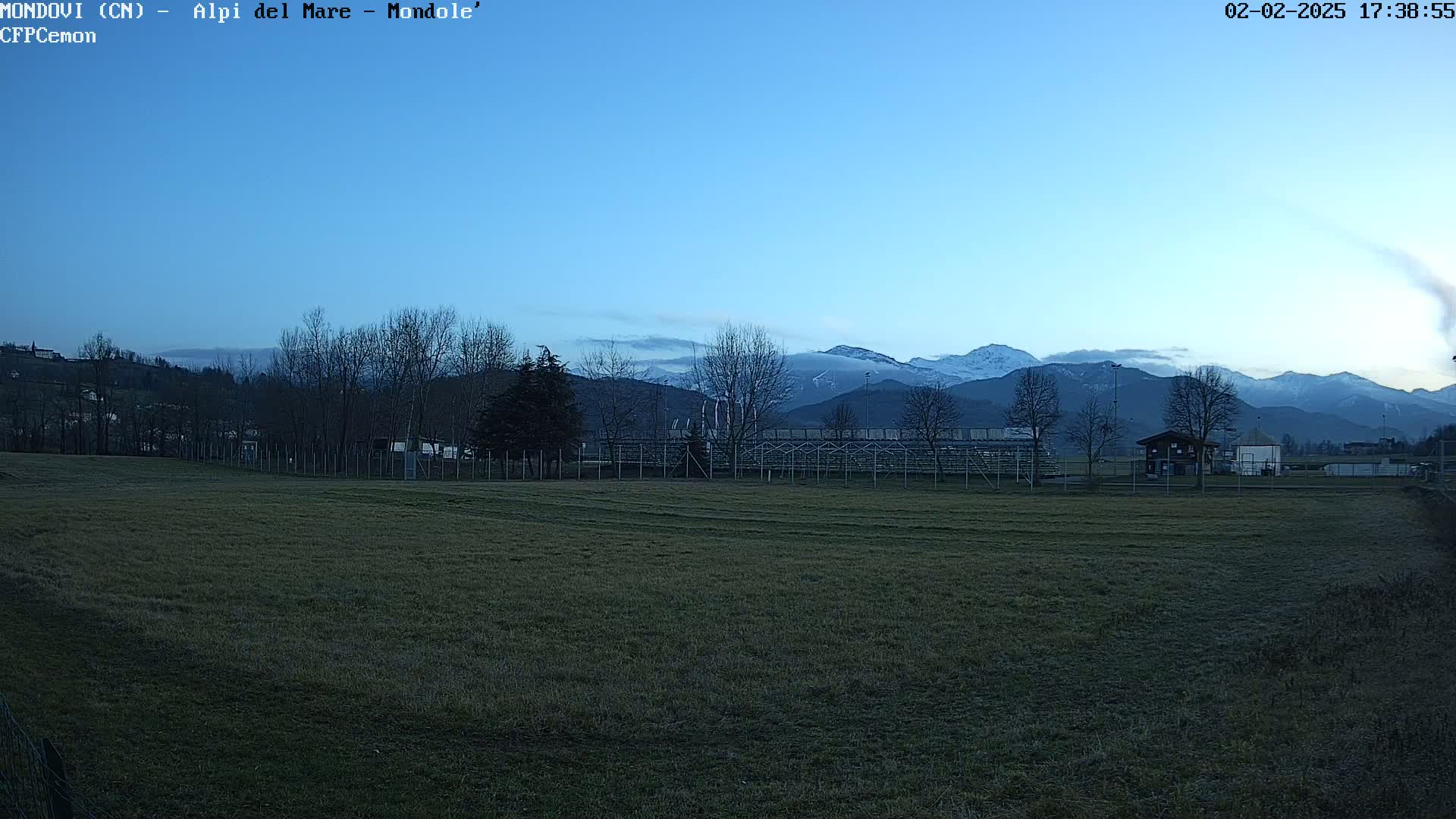A grassy field sits before a snow-capped mountain range under a clear, twilight sky.