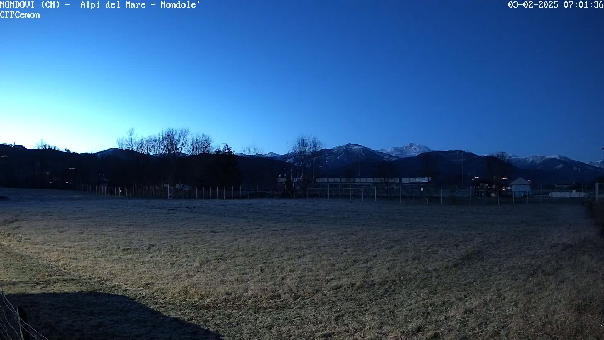 A field of brown grass stretches towards snow-capped mountains under a twilight blue sky.