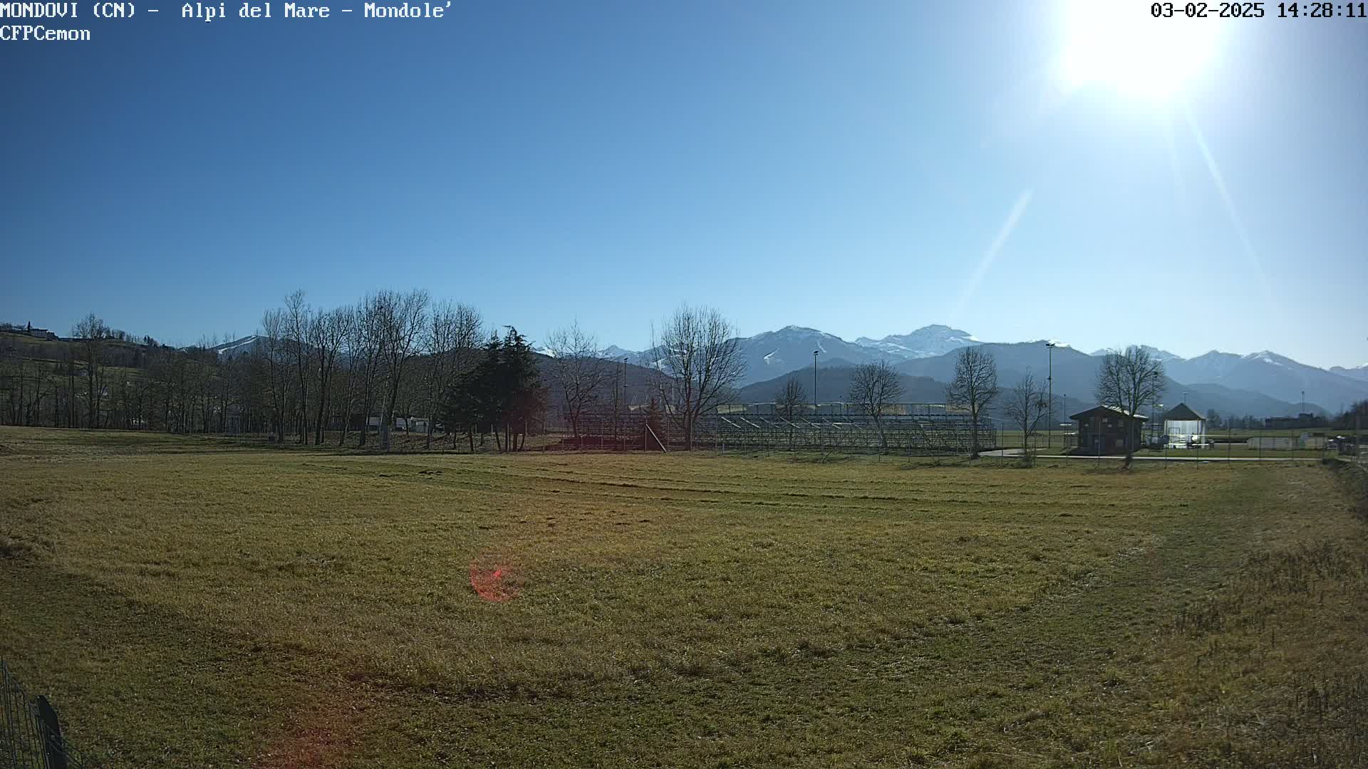 A sunny day reveals a grassy field, a small building, and a distant mountain range capped with snow.