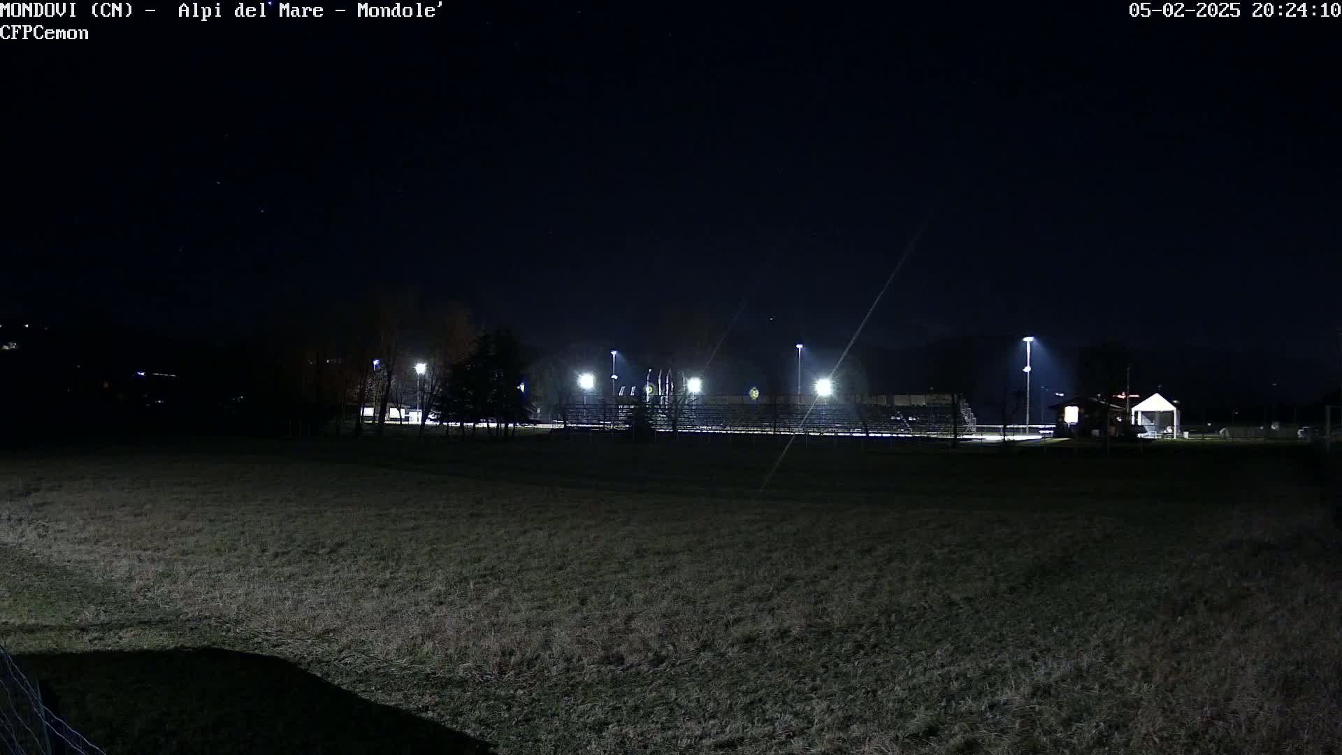 A nighttime view of an empty field with bleachers and lights illuminating a sports field under a clear, dark sky.