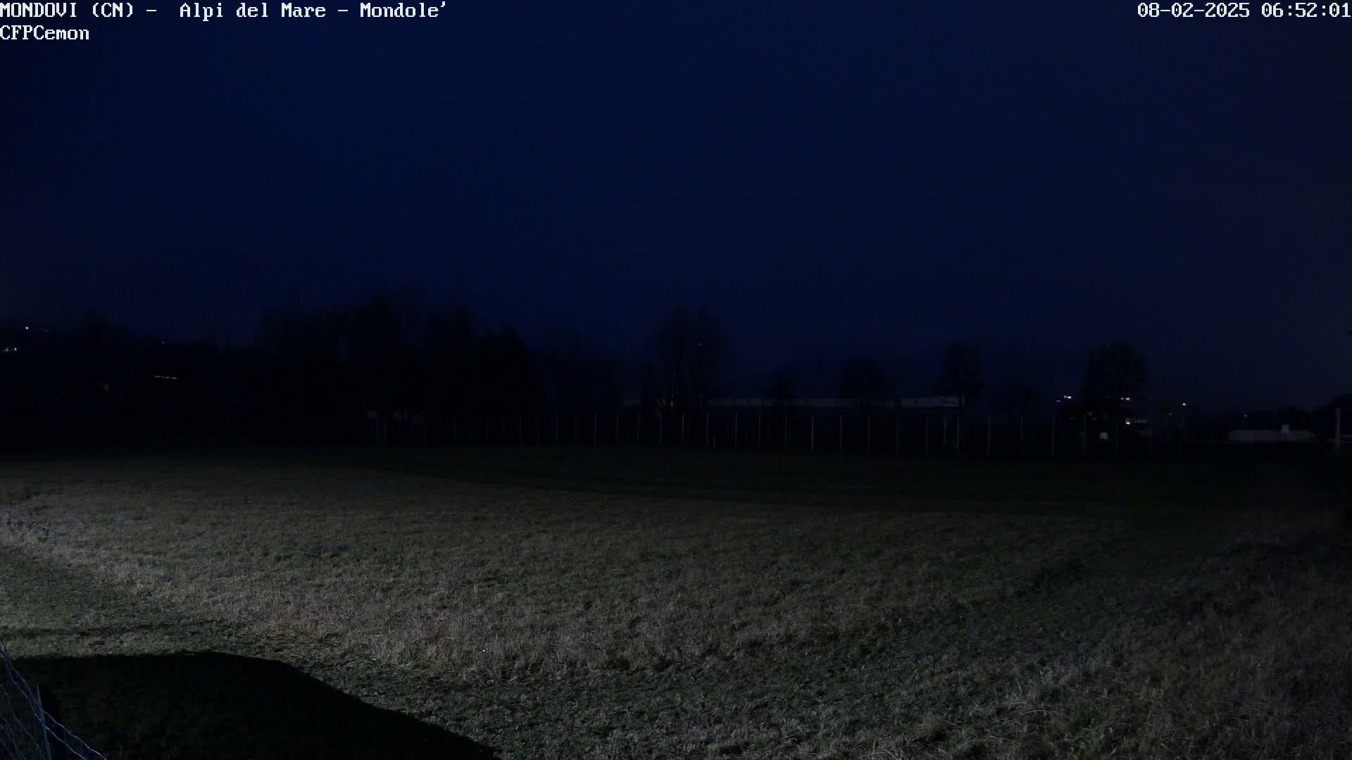 A dark, nighttime field is visible, bordered by a fence and trees under a clear, dark blue sky.