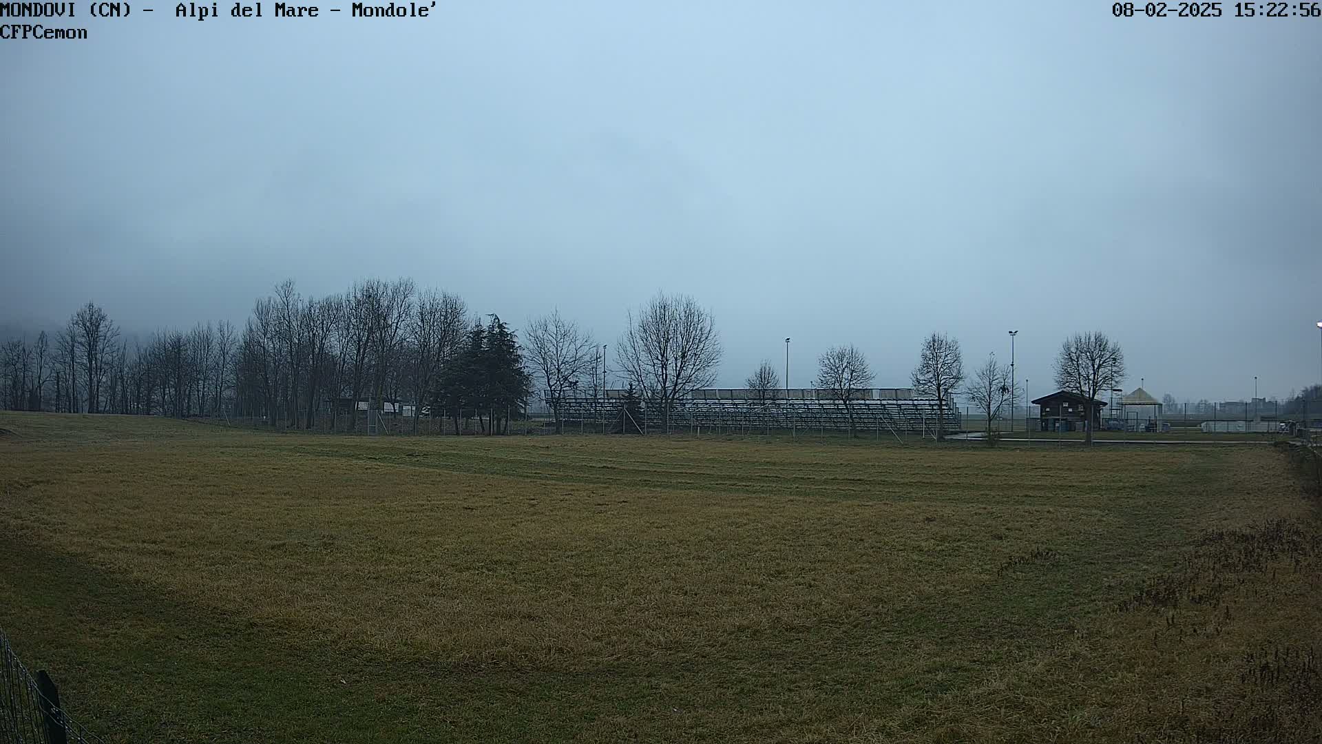 A mostly barren field stretches out before empty bleachers under a hazy, overcast sky.