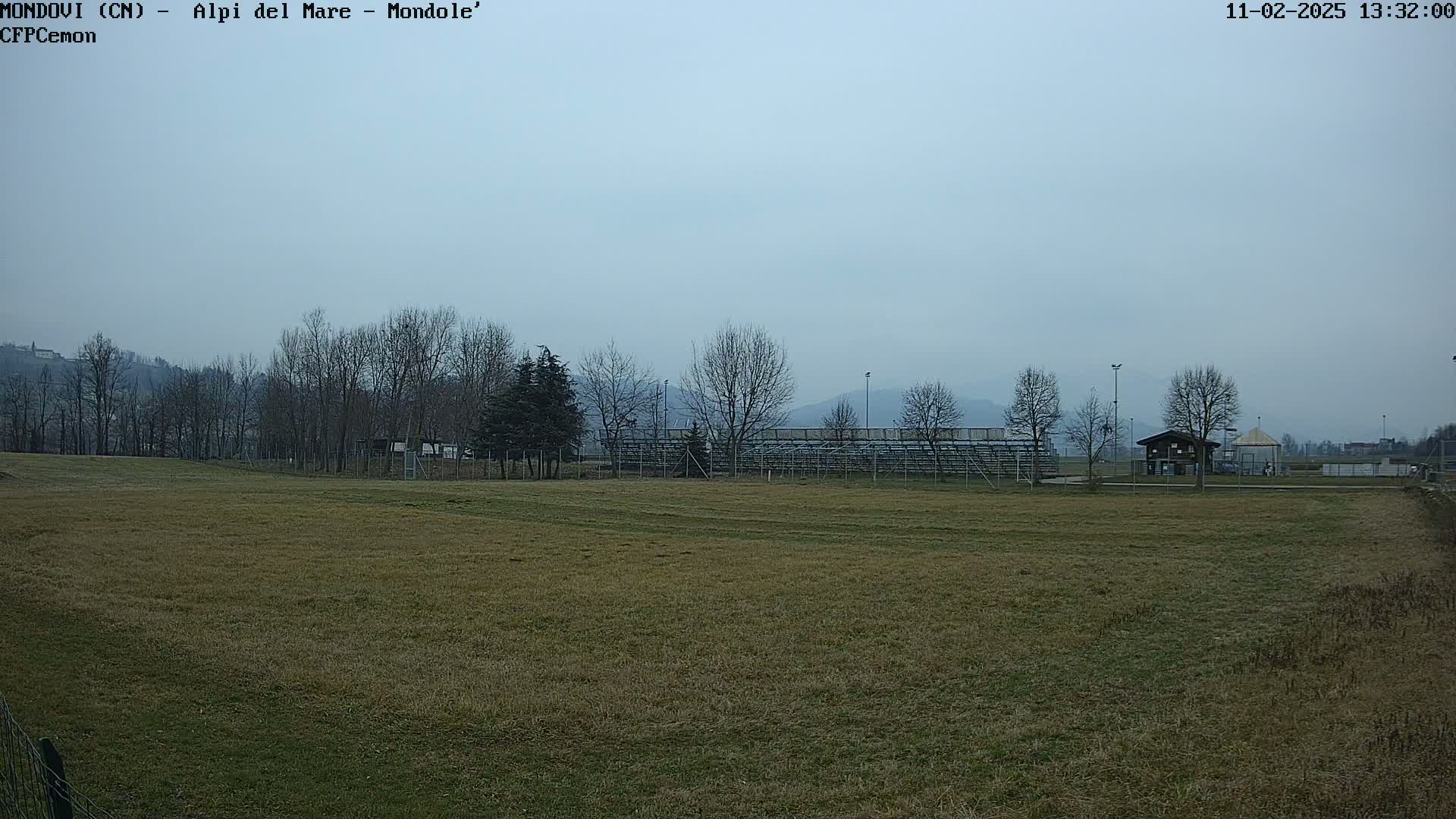 A grassy field with bleachers and a small building in the background under an overcast sky.