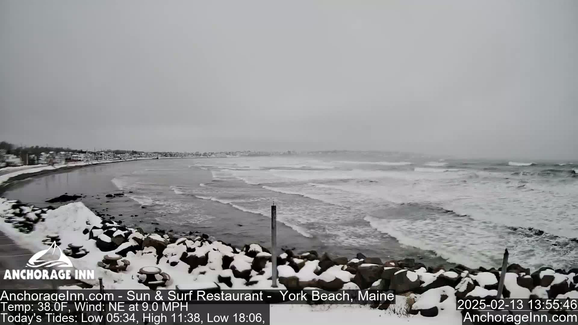 A snow-covered rocky shoreline meets a gray, choppy ocean under an overcast sky.