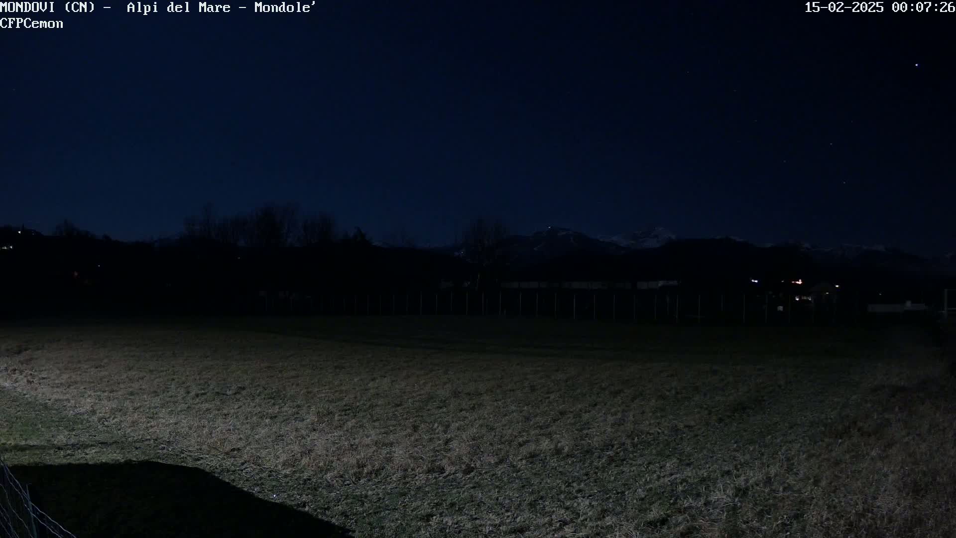 A dark field is illuminated at night under a clear, starry sky, with distant mountains visible on the horizon.