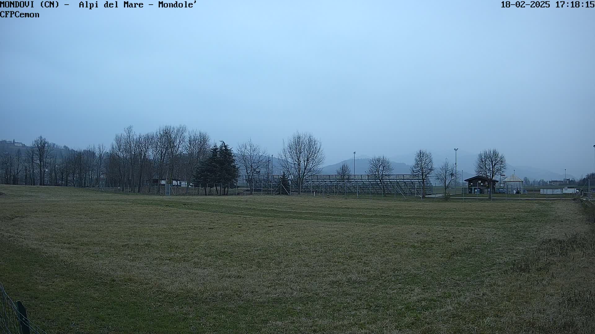 A mostly barren field with bleachers and a small building in the background under a hazy sky.