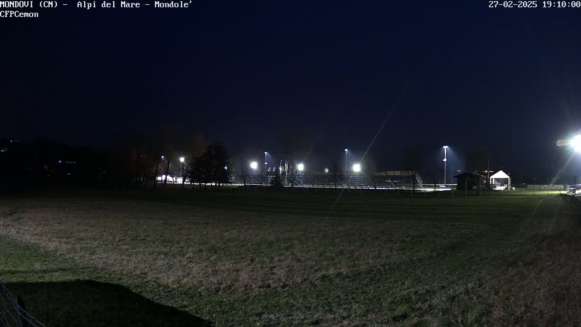 A nighttime view of a field with bleachers and lights in the background under a dark, clear sky.