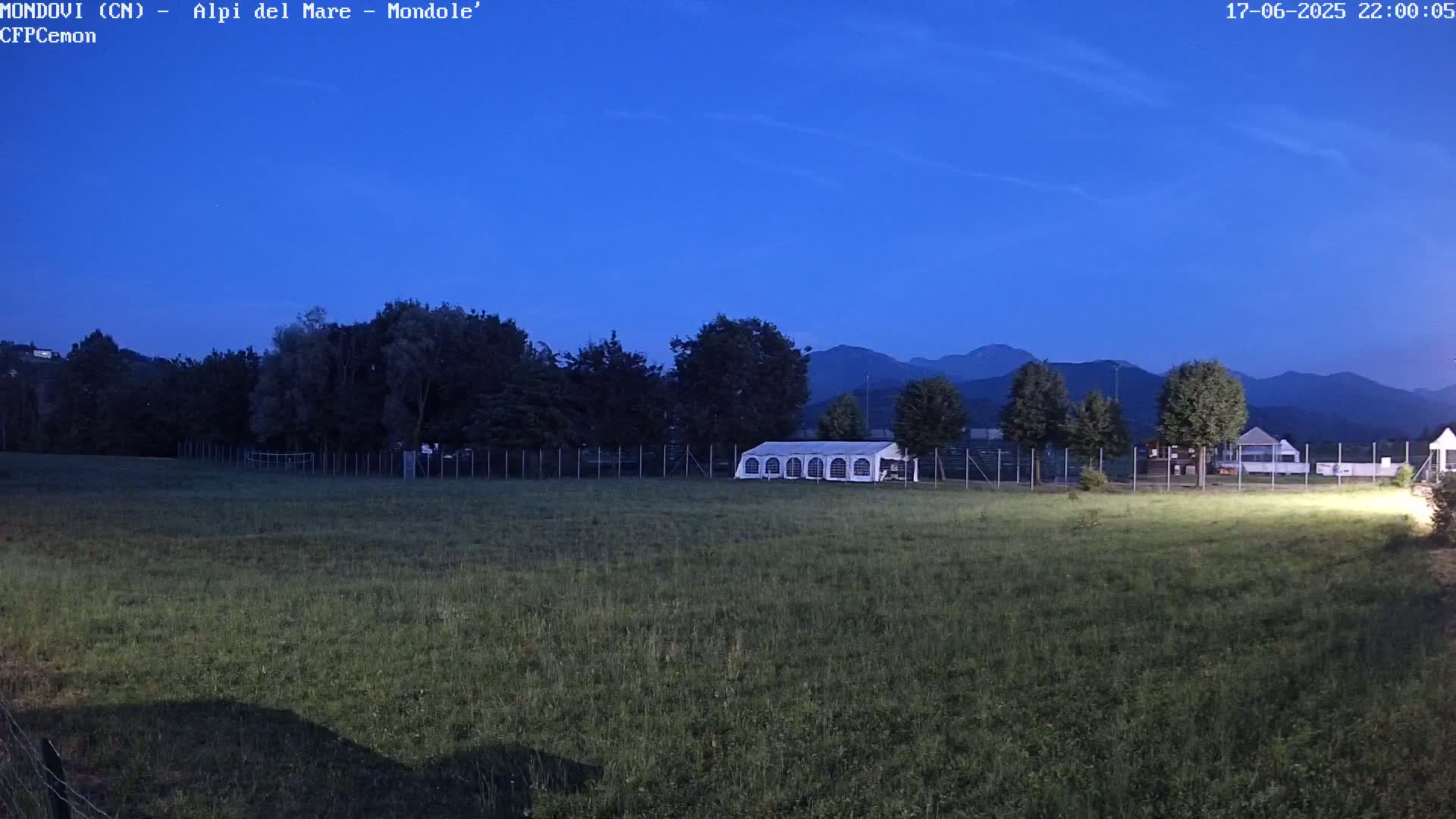A large white tent sits in a grassy field enclosed by a fence, under a twilight blue sky with mountains in the background.